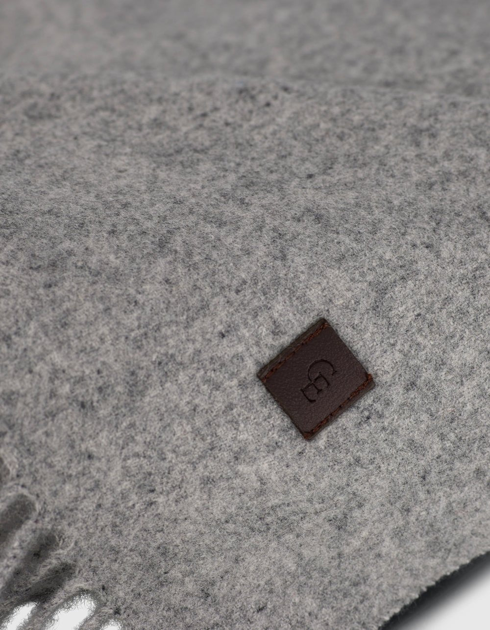 Close-up of Cozy Earth’s Cashmere Tassel Throw in soft light grey, showing its cozy texture. A small brown leather tag with an embossed logo is stitched on for a refined touch.