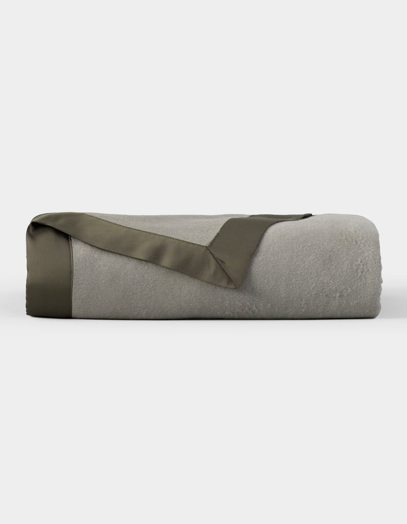 The Cozy Earth Bamboo Blanket, shown neatly folded with an olive green satin trim, is featured against a plain white background.
