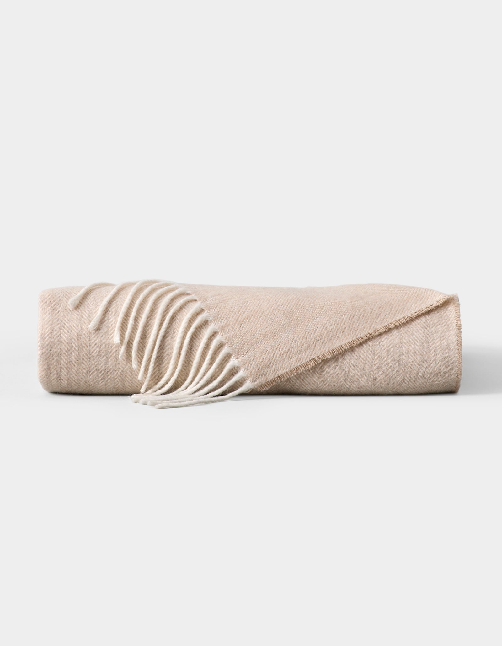 The Cozy Earth Bamboo Herringbone Tassel Throw is a folded beige blanket featuring a subtle herringbone pattern and white tassel fringe on one edge, displayed against a plain white background. 