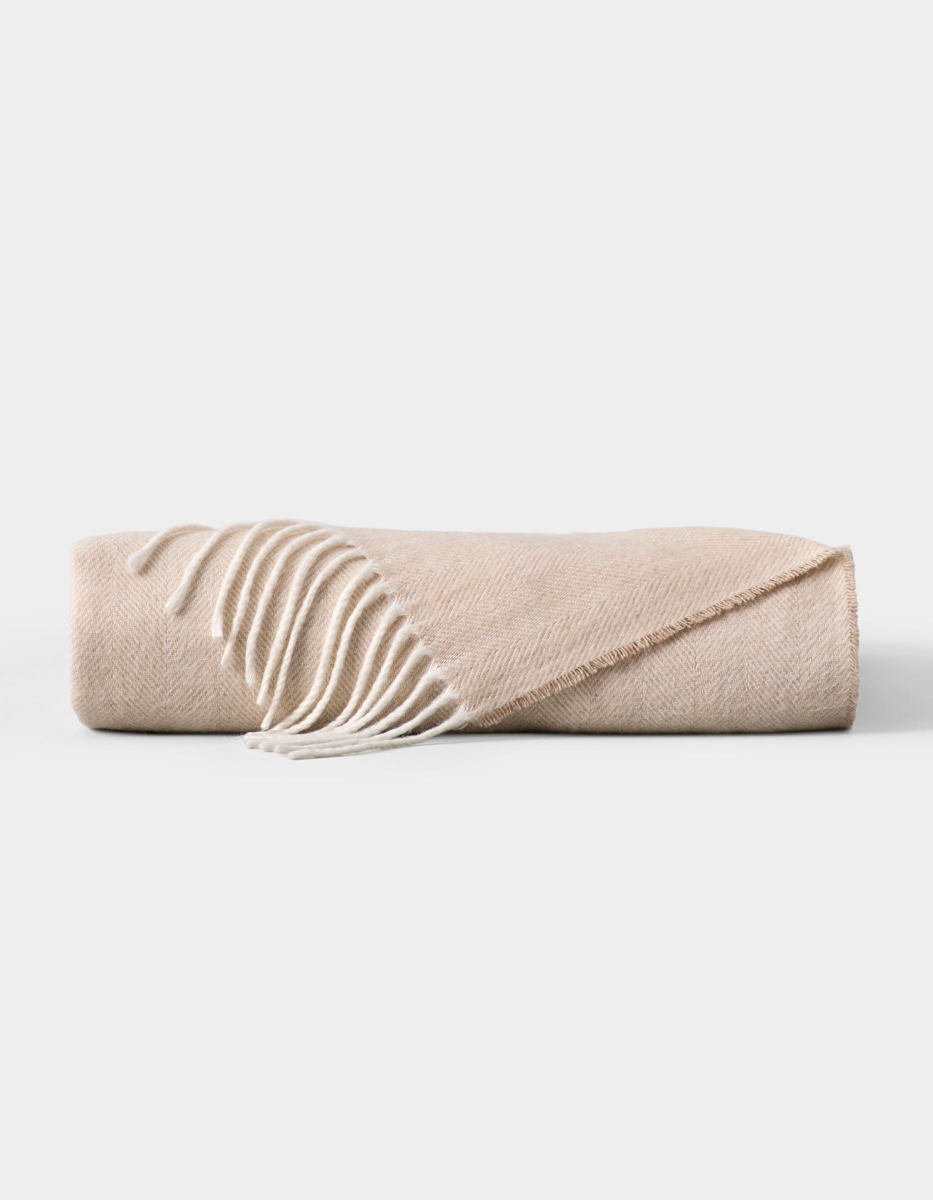The Cozy Earth Bamboo Herringbone Tassel Throw is a folded beige blanket featuring a subtle herringbone pattern and white tassel fringe on one edge, displayed against a plain white background. 