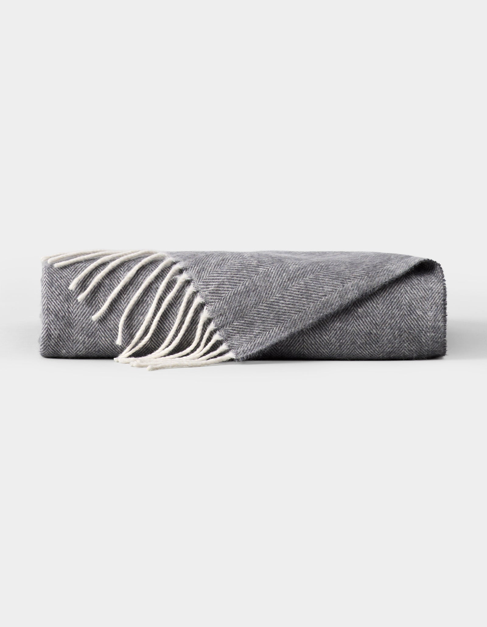 The Cozy Earth Bamboo Herringbone Tassel Throw is a folded gray blanket with white fringed tassels along one edge, shown on a plain white background. 