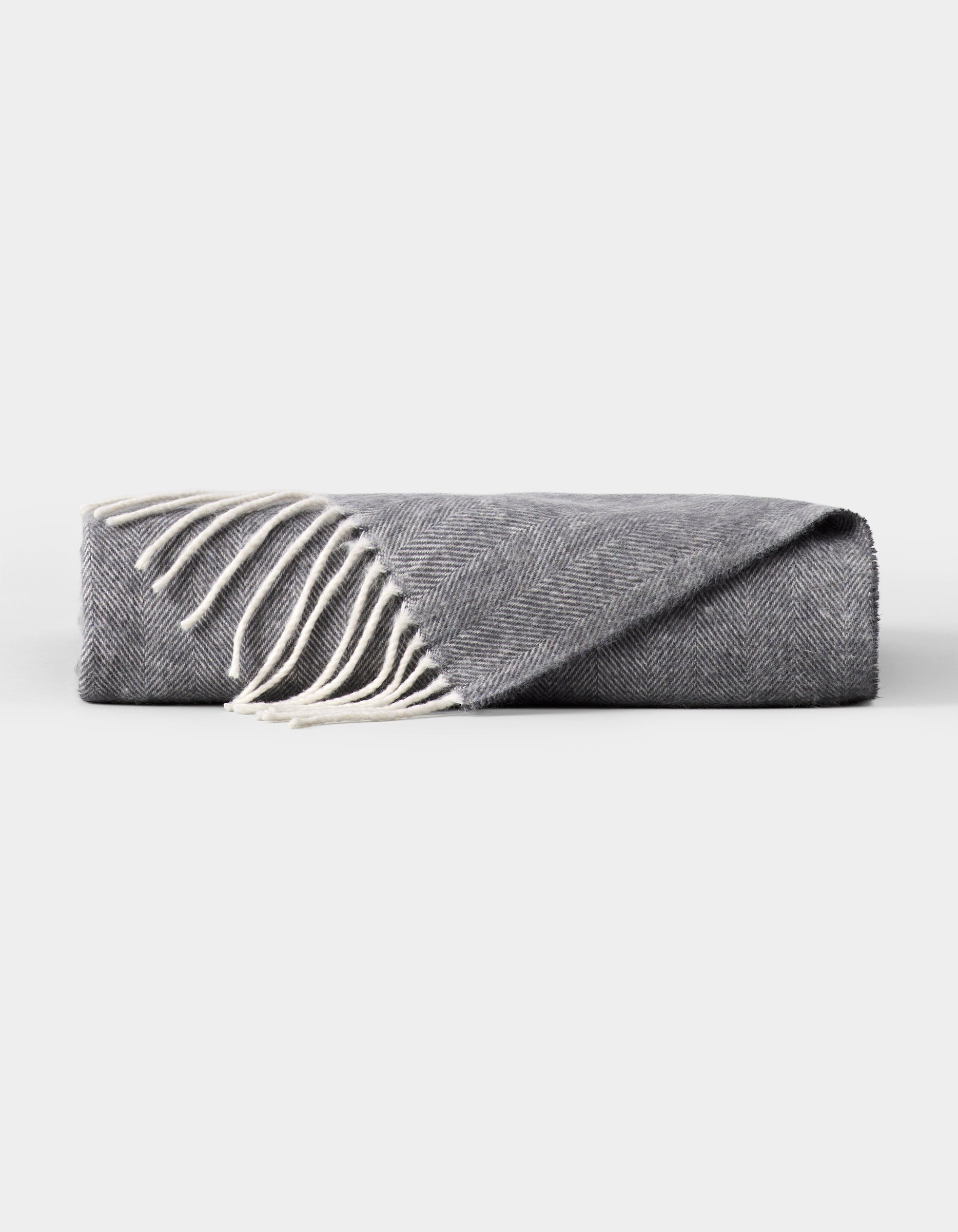The Cozy Earth Bamboo Herringbone Tassel Throw is a folded gray blanket with white fringed tassels along one edge, shown on a plain white background. 
