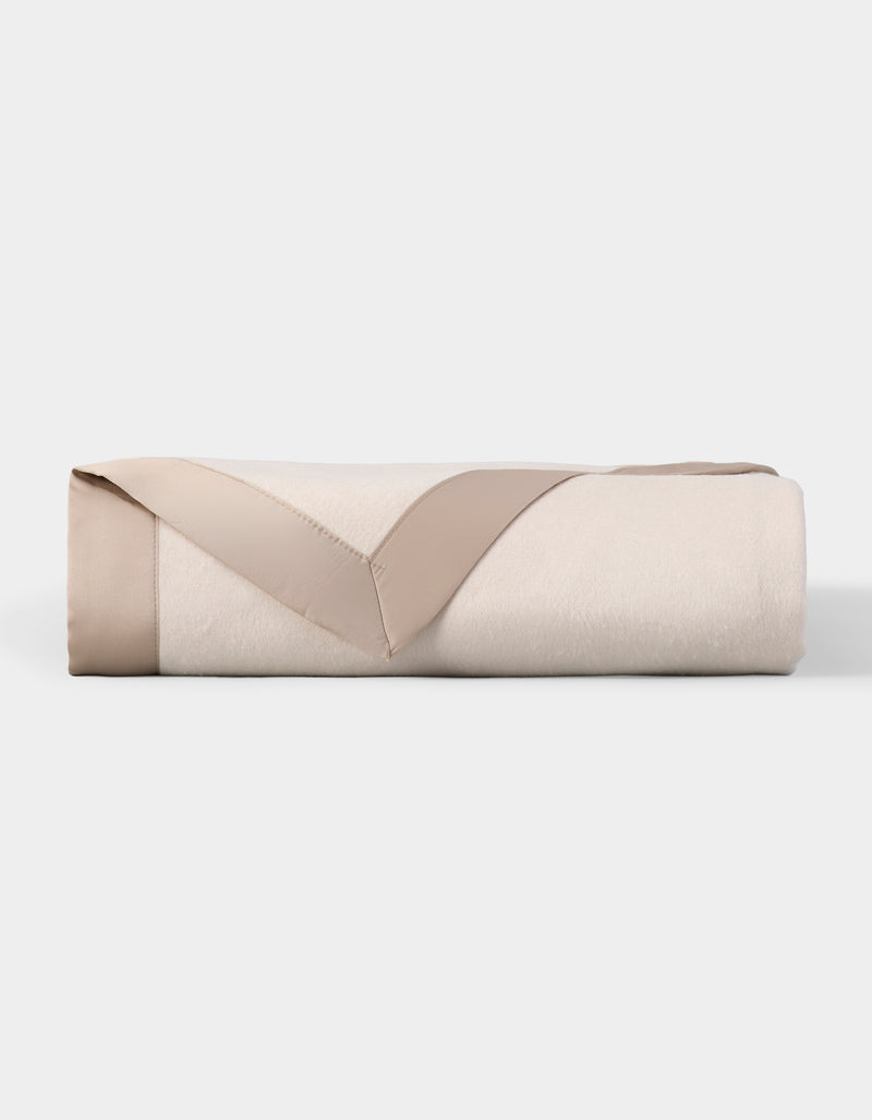 The Cozy Earth Bamboo Blanket is neatly folded, cream-colored with a beige satin trim, and displayed on a plain white background.