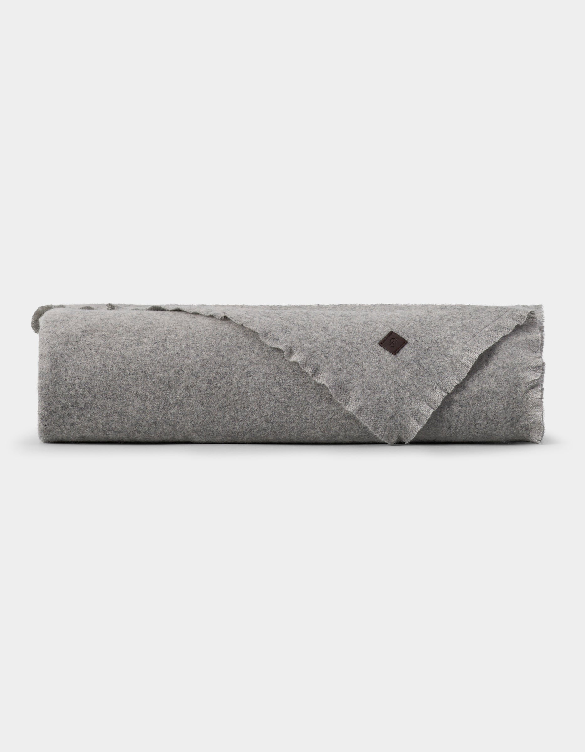 A neatly folded light gray Cozy Earth Cashmere Fringe Blanket with a small dark brown patch on one corner, displayed against a plain white background.