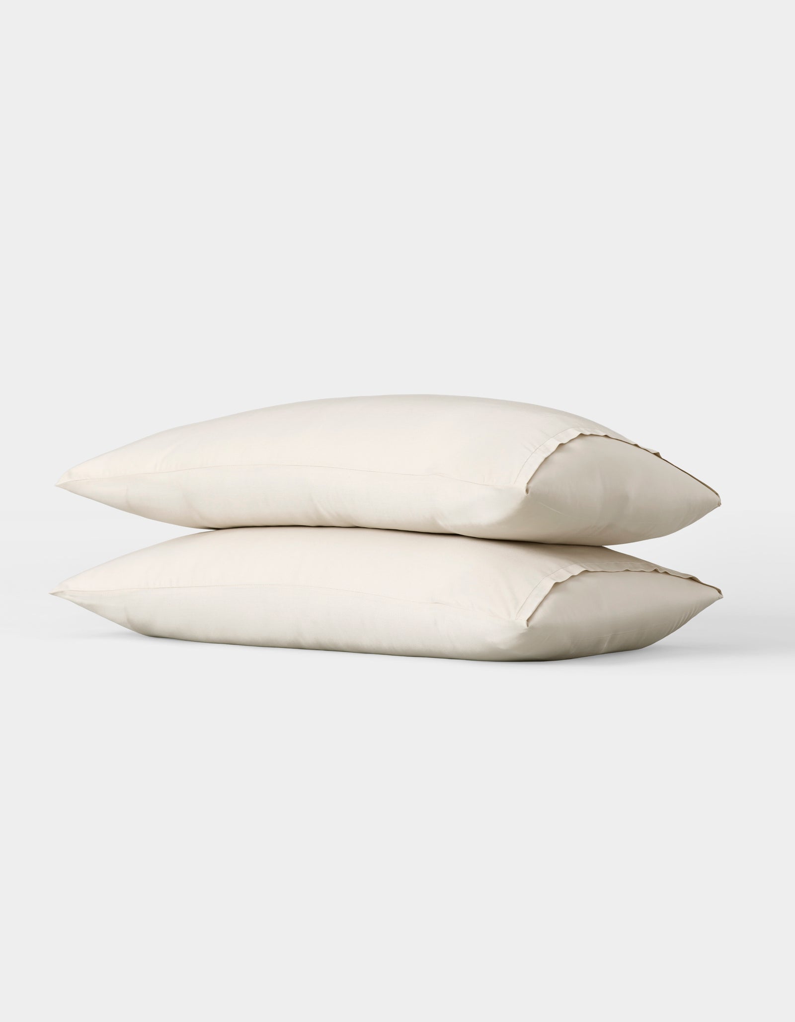 Two Bamboo Pillowcases by Cozy Earth, plain white, are stacked together against a simple light gray background. 
