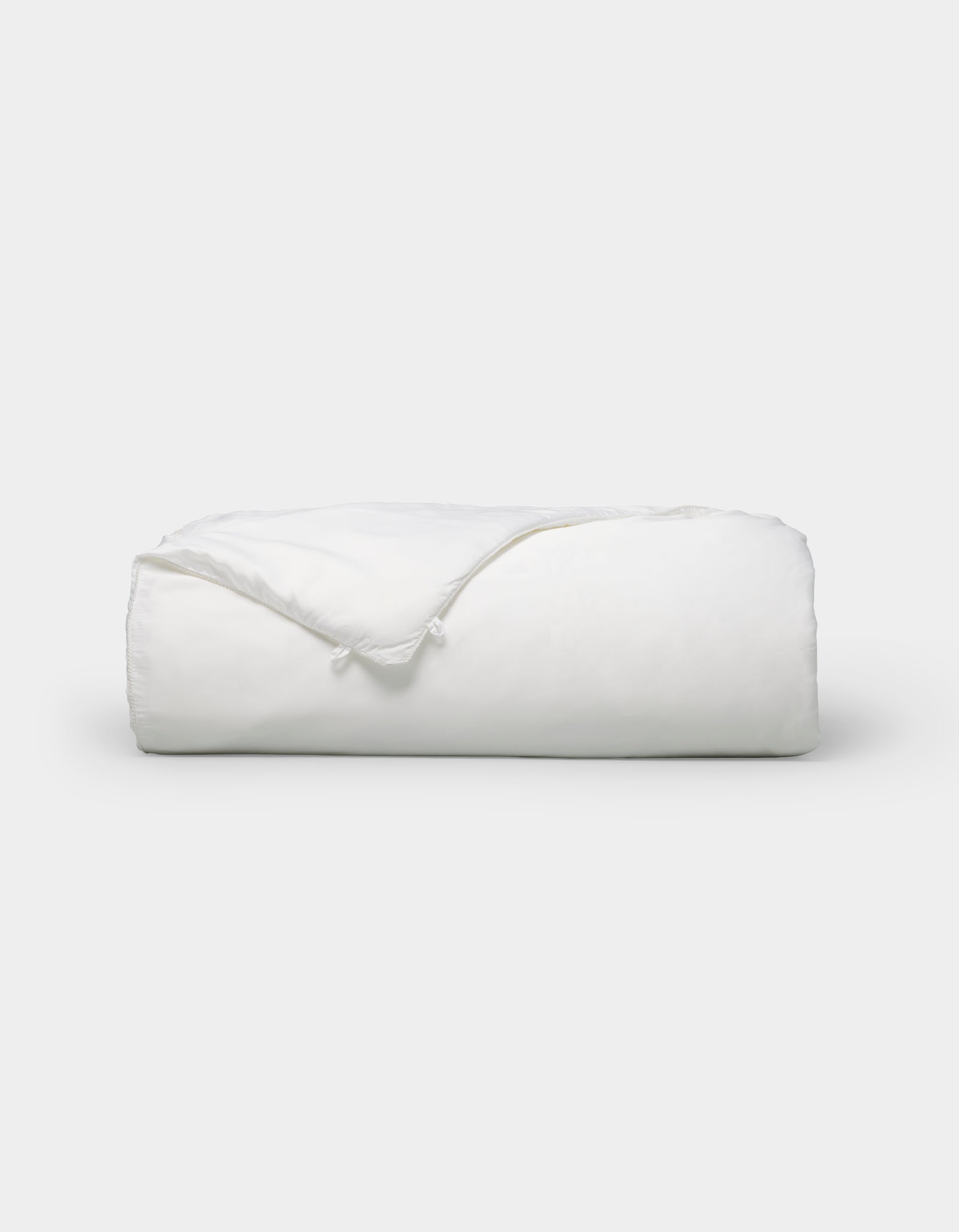 The Cozy Earth Silk Insert Bundle is a neatly folded white comforter with visible corner and tied fabric loops, shown against a plain white background.