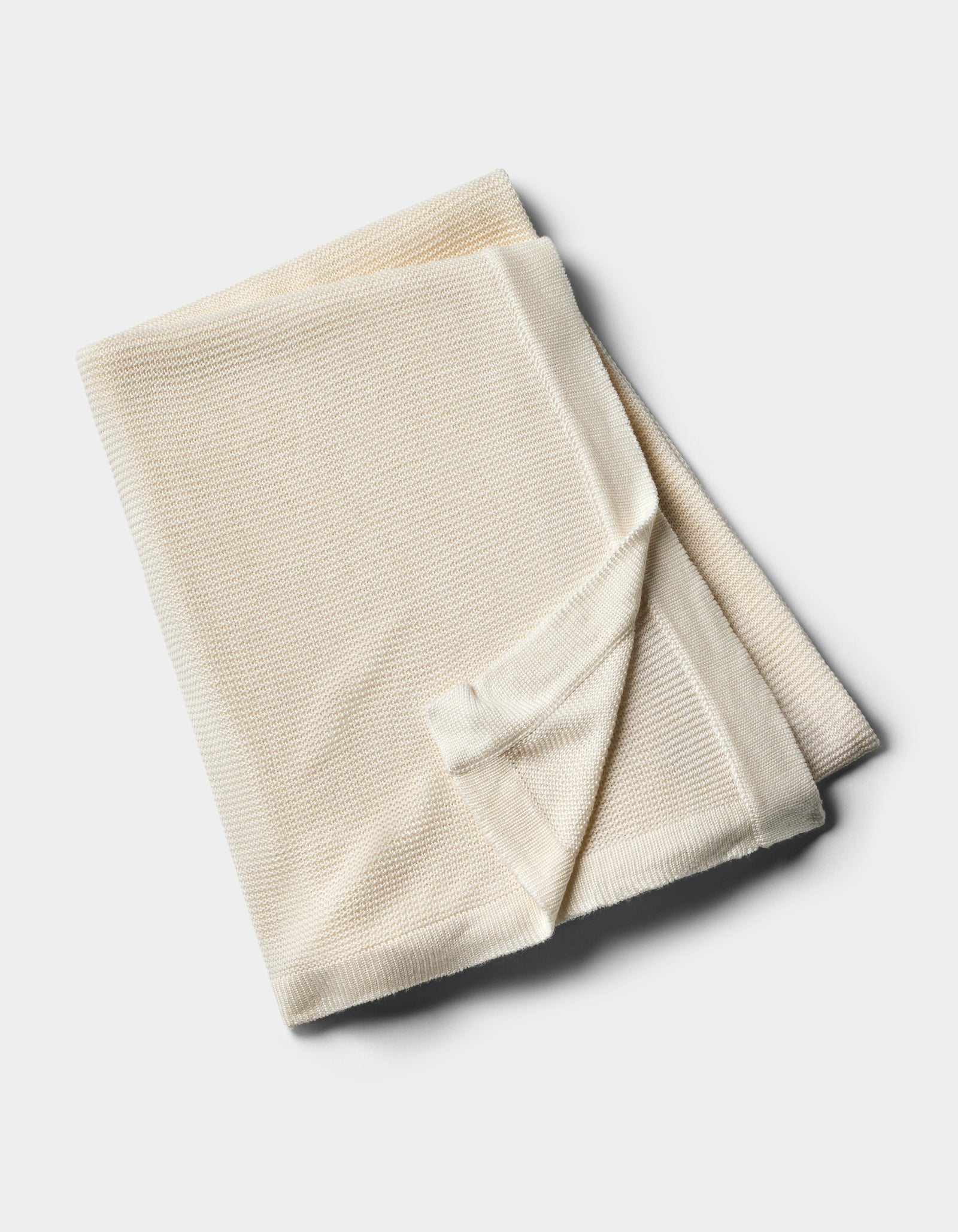 The Cozy Earth Cloud Knit Blanket by Cozy Earth, in a cream hue, is neatly folded and displayed on a plain white background.
