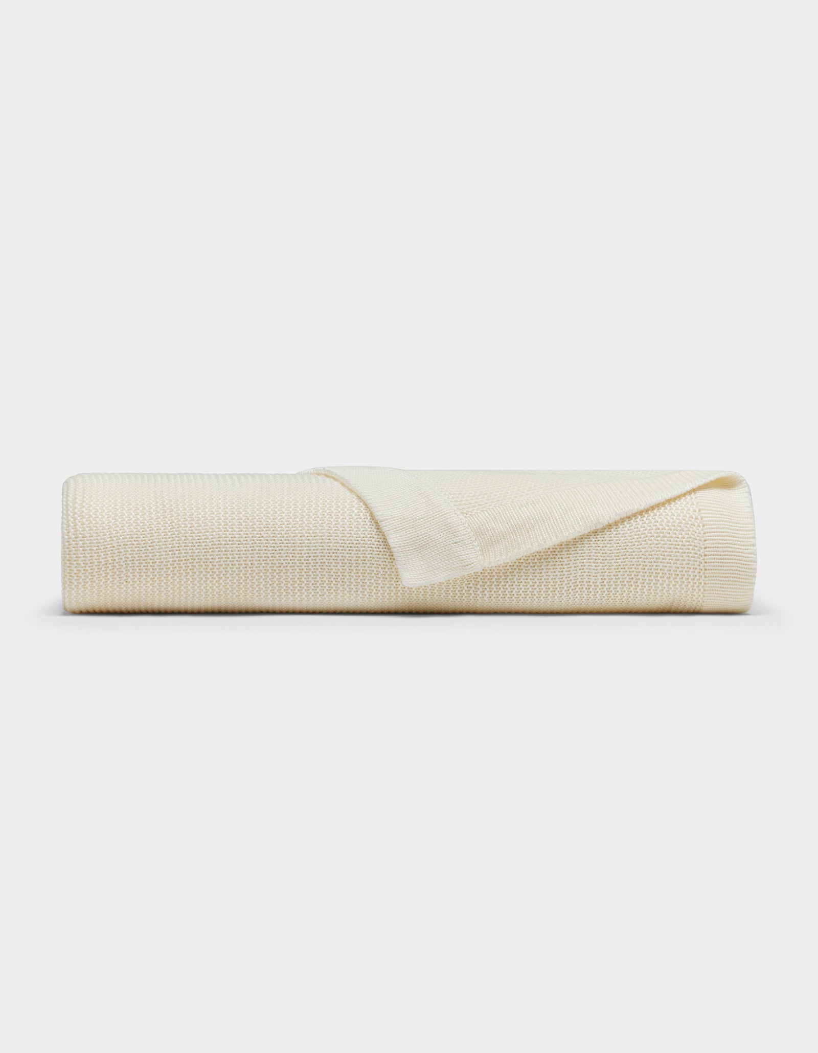 The Cozy Earth Cloud Knit Blanket by Cozy Earth is cream-colored with a textured pattern, neatly rolled and displayed on a white background. One edge is folded back, highlighting the blanket's thickness and texture.