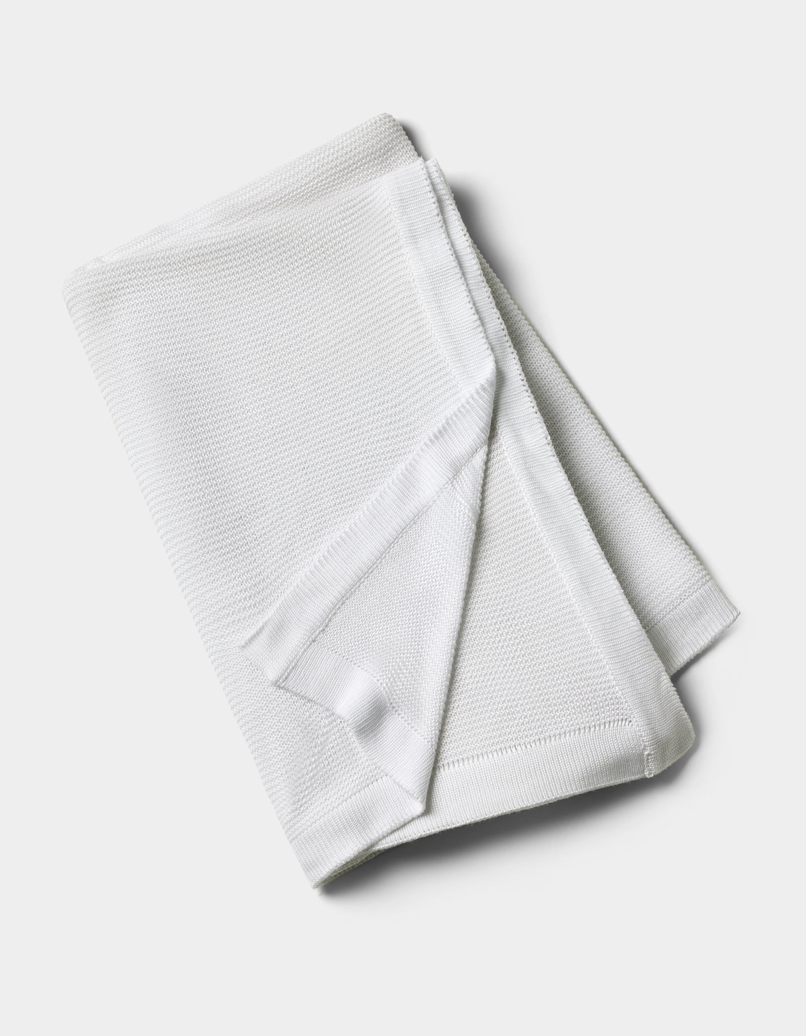 The Cozy Earth Cloud Knit Blanket by Cozy Earth is neatly folded and displayed on a plain, light background, showcasing its white textured fabric.
