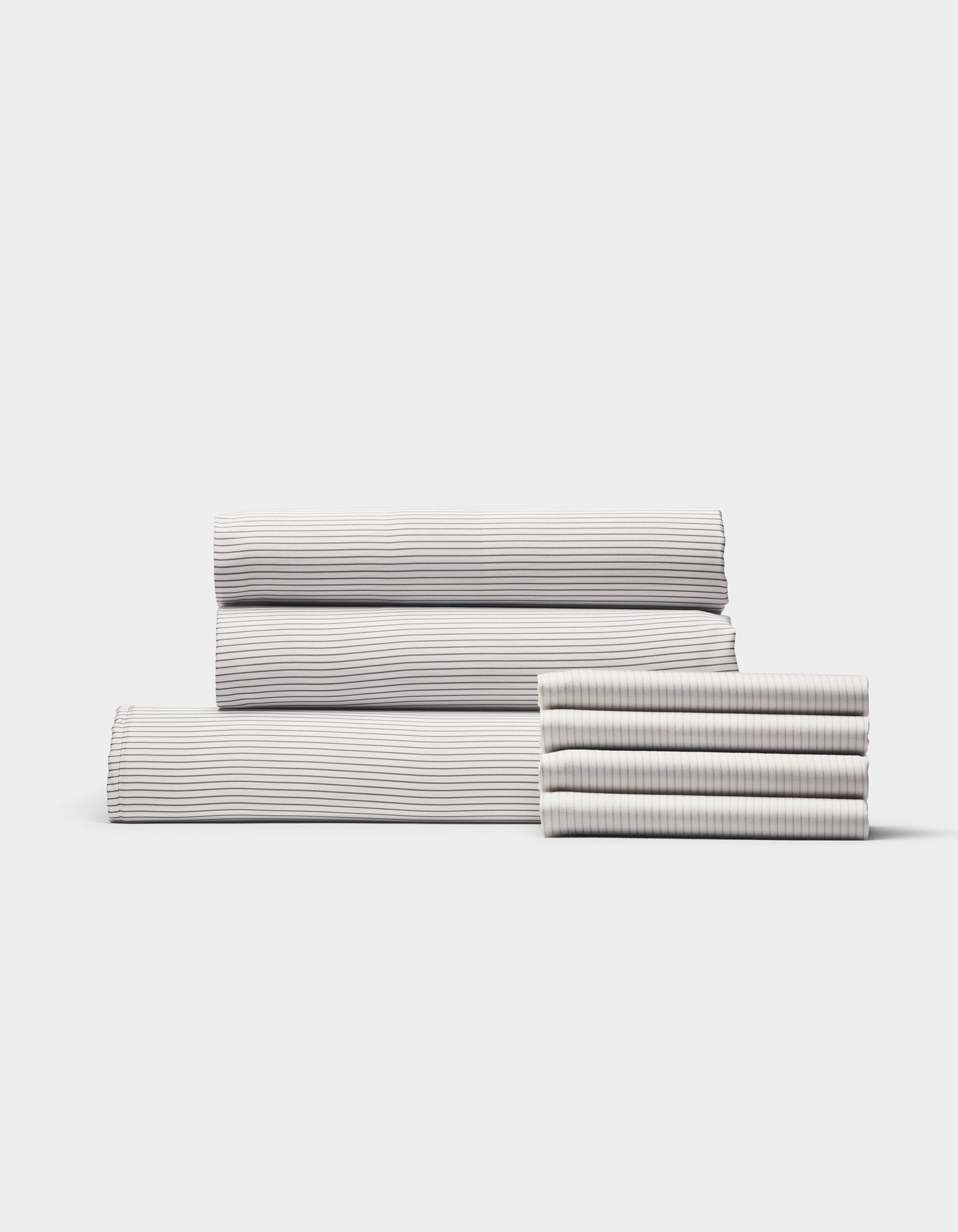 The Bamboo Bedding Core Bundle by Cozy Earth features neatly folded bed sheets and pillowcases with subtle, thin horizontal stripes in light and dark tones, all displayed against a plain white background.