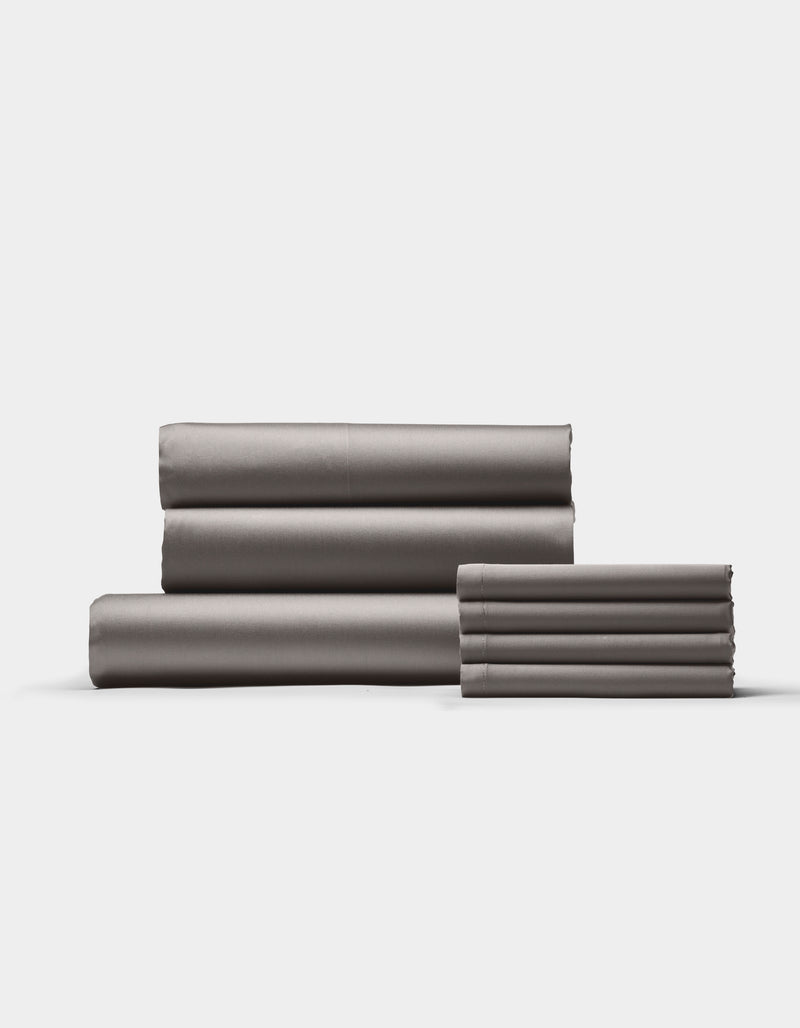 The Cozy Earth Bamboo Bedding Core Bundle features neatly folded gray bed sheets arranged in two stacks against a plain white background.