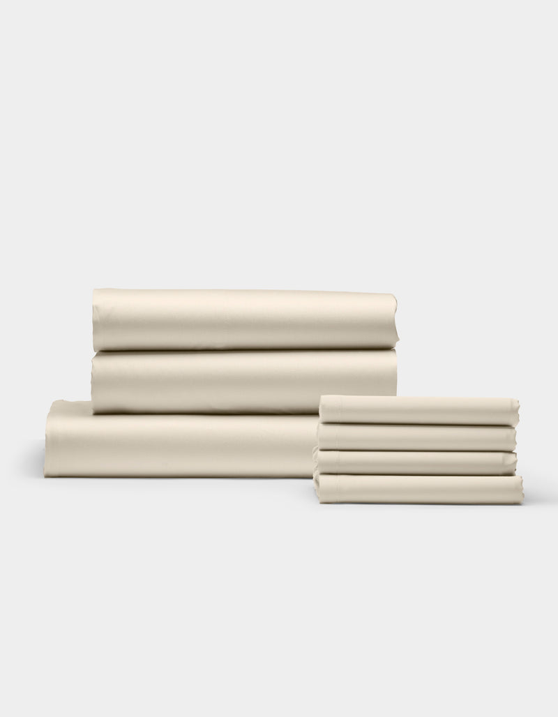 The Cozy Earth Bamboo Bedding Core Bundle, featuring cream-colored bed sheets and pillowcases, is neatly folded in two stacks against a plain white background.