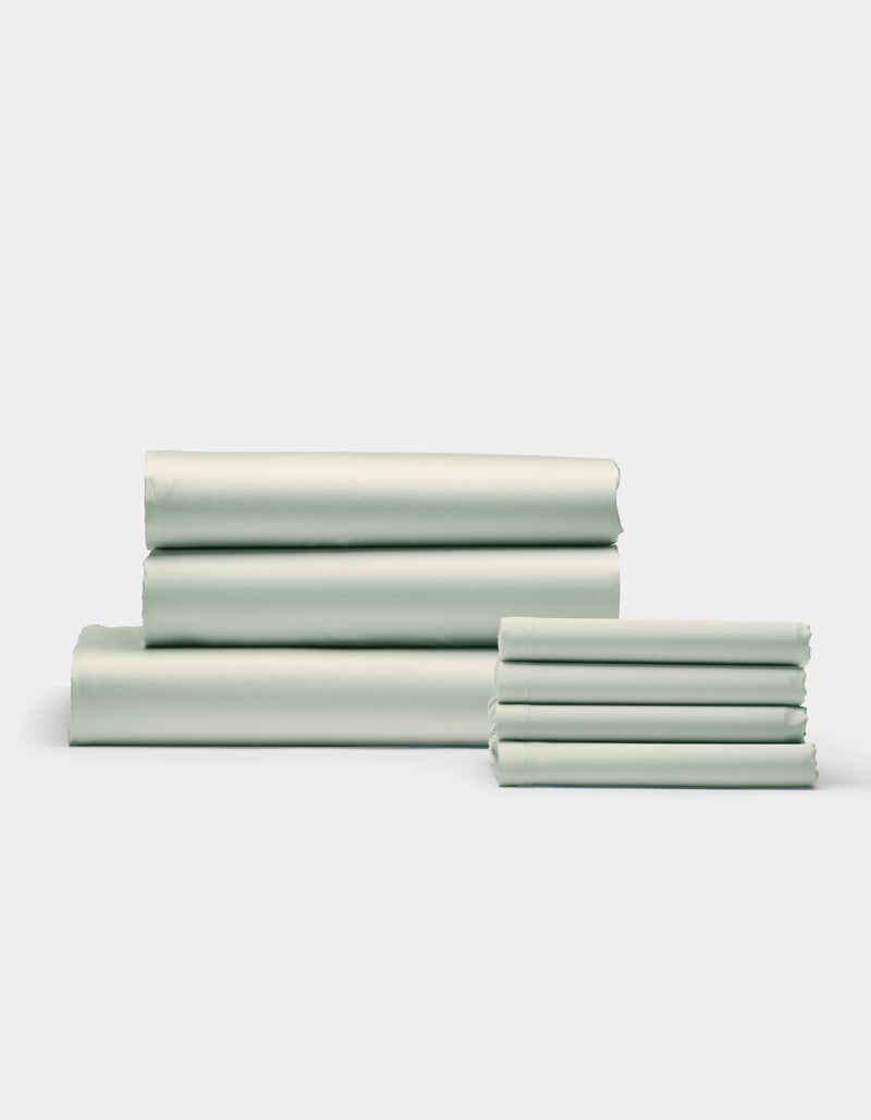 Cozy Earth's Bamboo Bedding Core Bundle, featuring neatly folded light green bed sheets and pillowcases, is stacked in two groups against a plain white background.