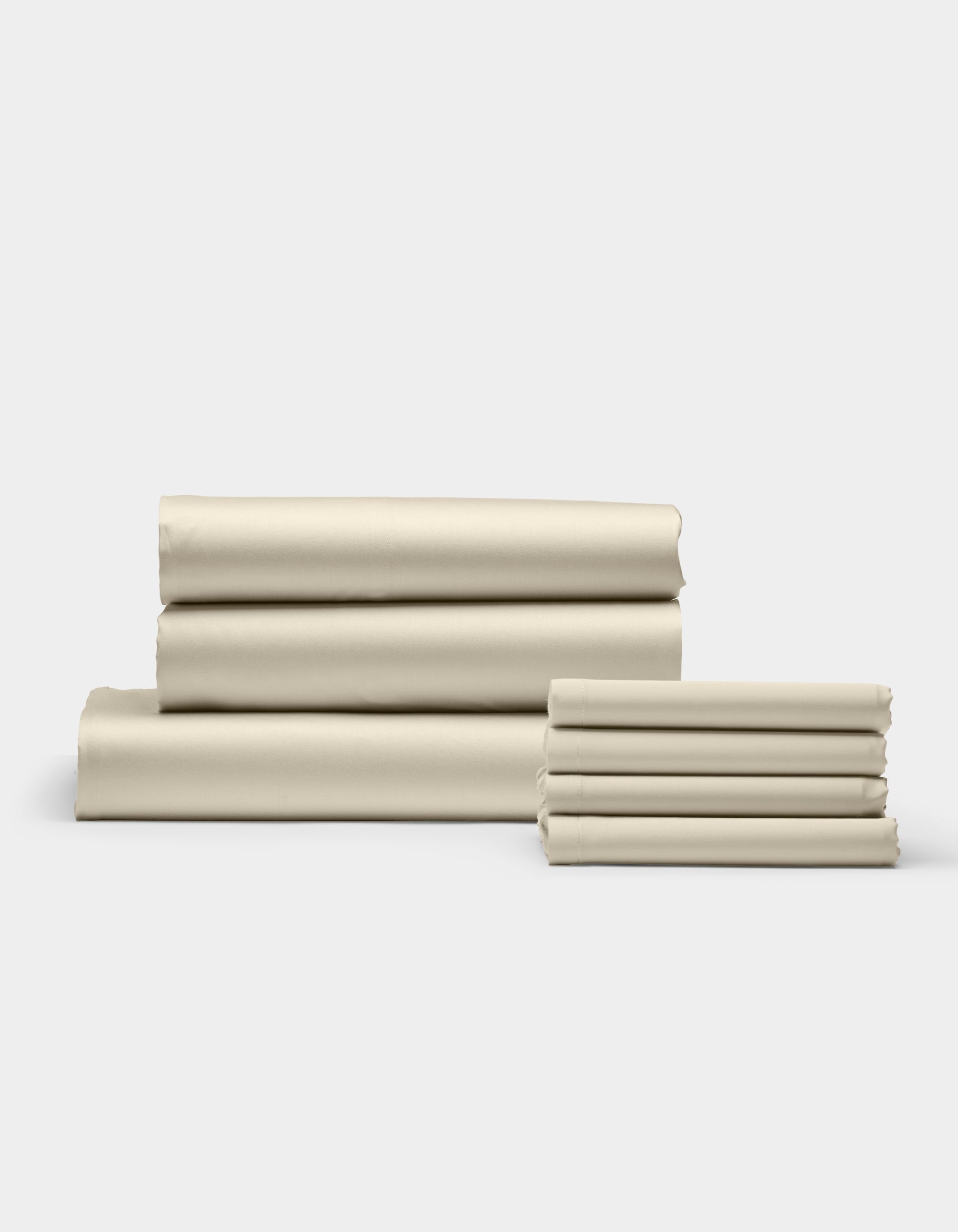 Cozy Earth’s Bamboo Bedding Core Bundle is shown in stacks of neatly folded beige sheets, arranged on a white surface with a light gray background. The smooth sheets are organized into one large and one small pile.|Color:Oat