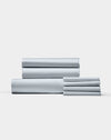 The Bamboo Bedding Core Bundle by Cozy Earth features neatly folded light gray bed sheets and pillowcases stacked against a plain white background.|Color:Shore