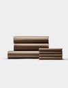 The Cozy Earth Bamboo Bedding Core Bundle is shown neatly stacked on a light background, featuring brown bed sheets and pillowcases—both large and small pieces are folded and displayed side by side.|Color:Walnut