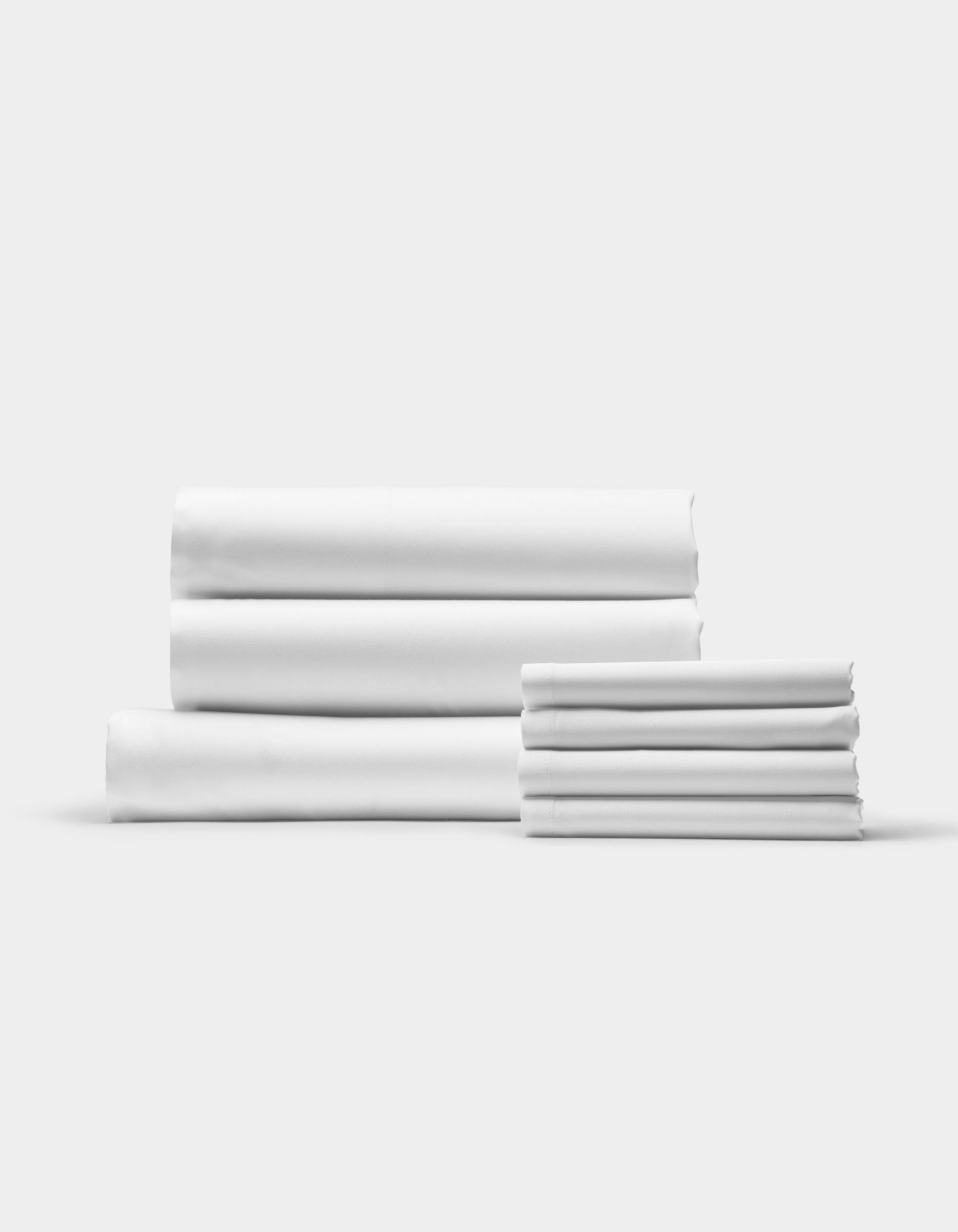 The Bamboo Bedding Core Bundle by Cozy Earth is displayed in two neat stacks against a plain white background, showcasing clean, unused linens with the larger stack on the left and a smaller stack on the right.|Color:White