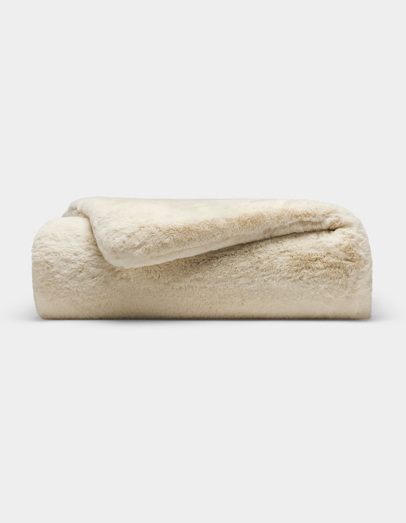 The Cozy Earth Cuddle Blanket, a plush cream-colored faux fur throw, is neatly folded and displayed against a plain white background.