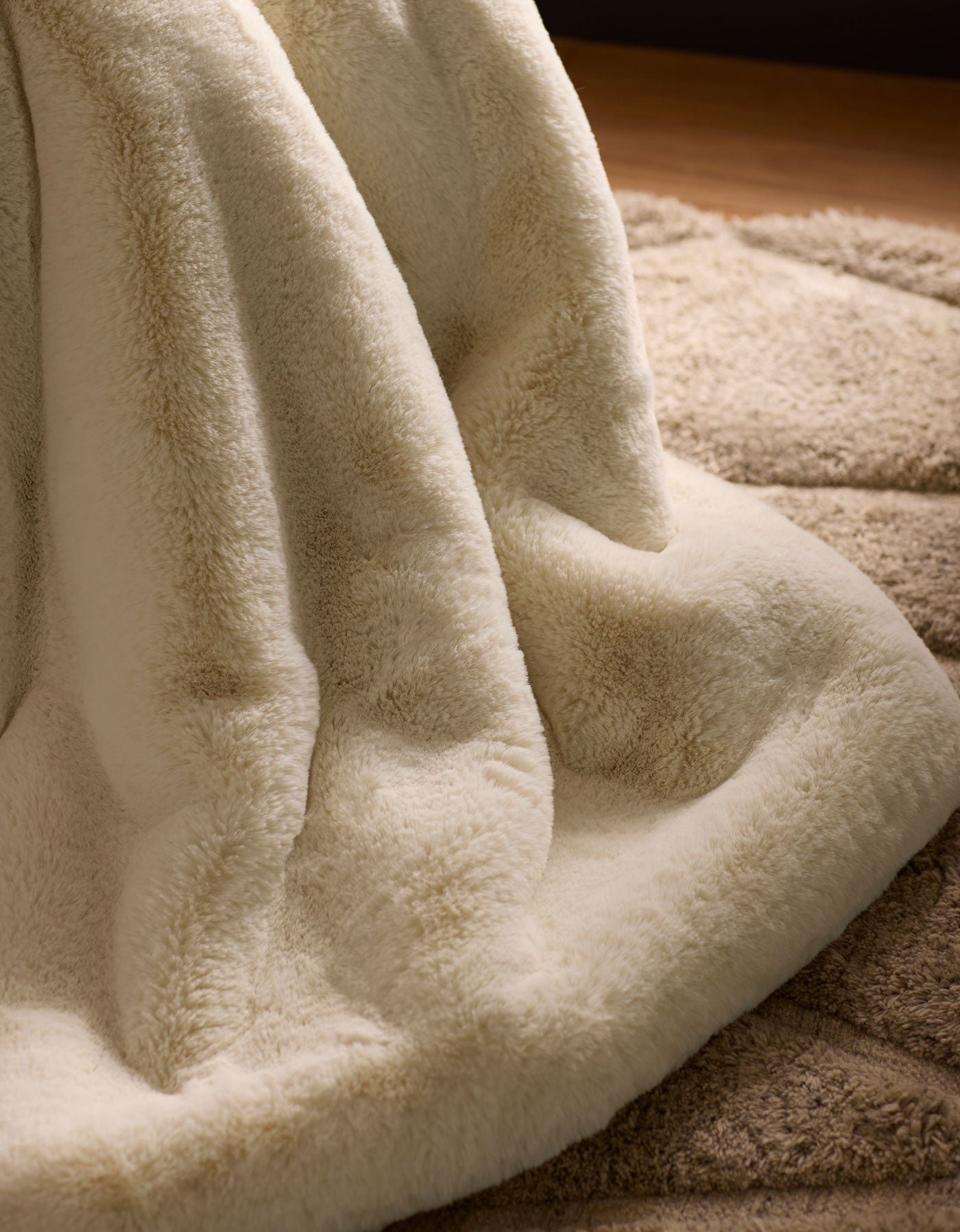 A close-up of the Cozy Earth Cuddle Blanket in cream, draped over a beige textured rug, creates a warm and cozy atmosphere.