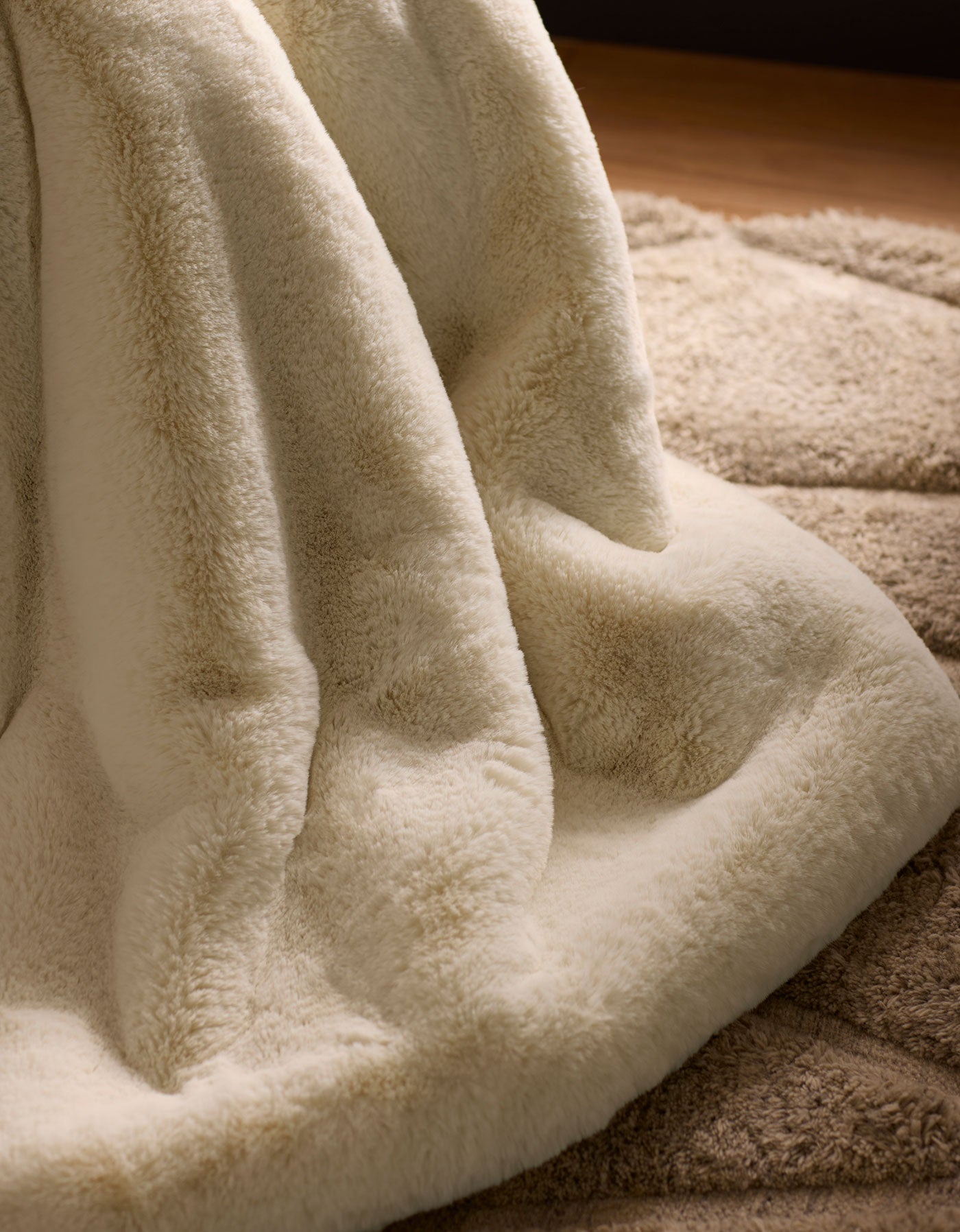 A close-up of the Cozy Earth Cuddle Blanket in cream, draped over a beige textured rug, creates a warm and cozy atmosphere.
