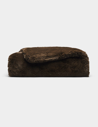 A folded, thick Cuddle Blanket by Cozy Earth in dark brown faux fur rests on a plain light gray background.|Color:Espresso