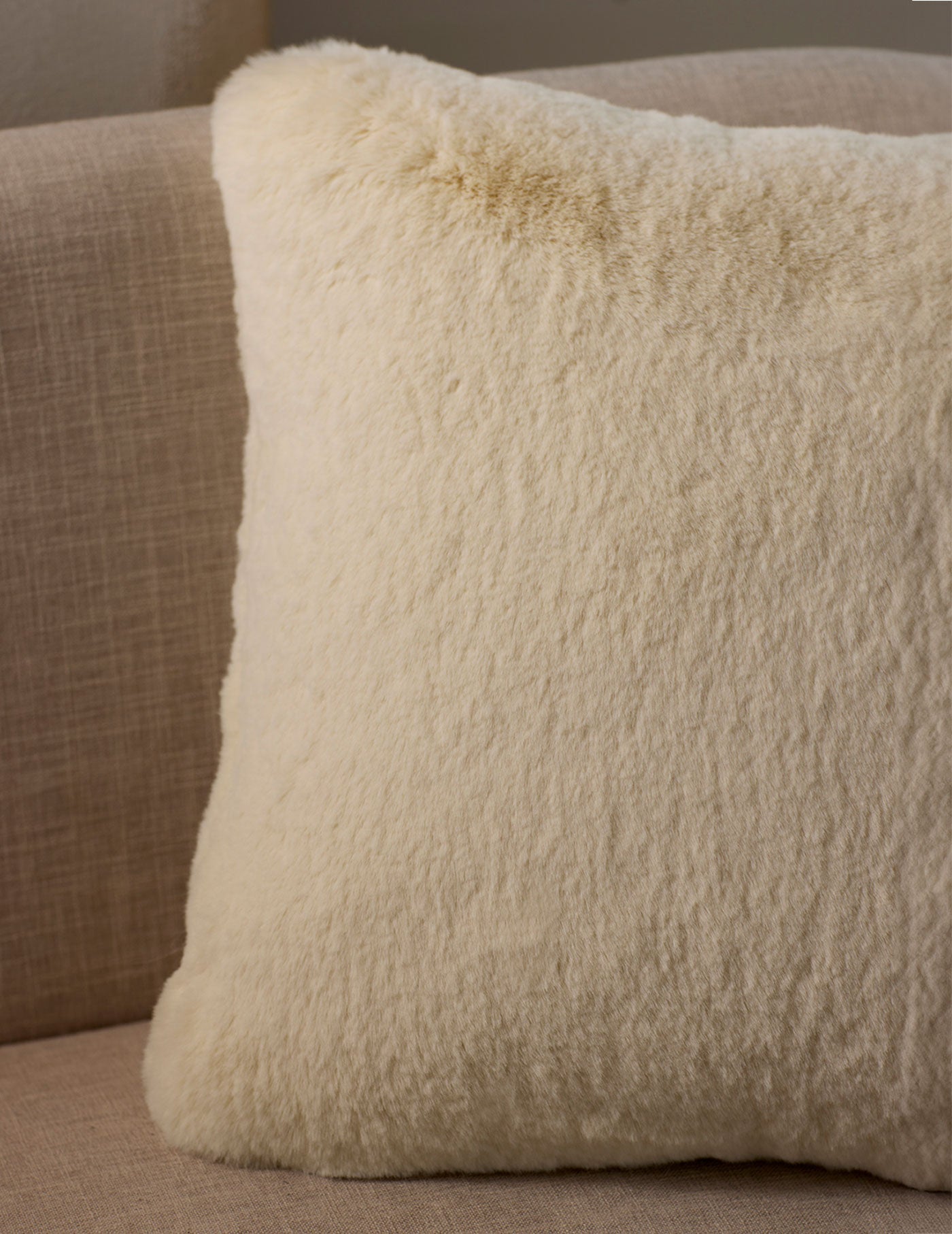 A close-up of the Cuddle Pillow by Cozy Earth, featuring a fluffy cream color and soft texture, placed on a light beige fabric sofa.