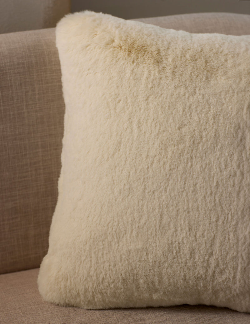 A close-up of the Cuddle Pillow by Cozy Earth, featuring a fluffy cream color and soft texture, placed on a light beige fabric sofa.