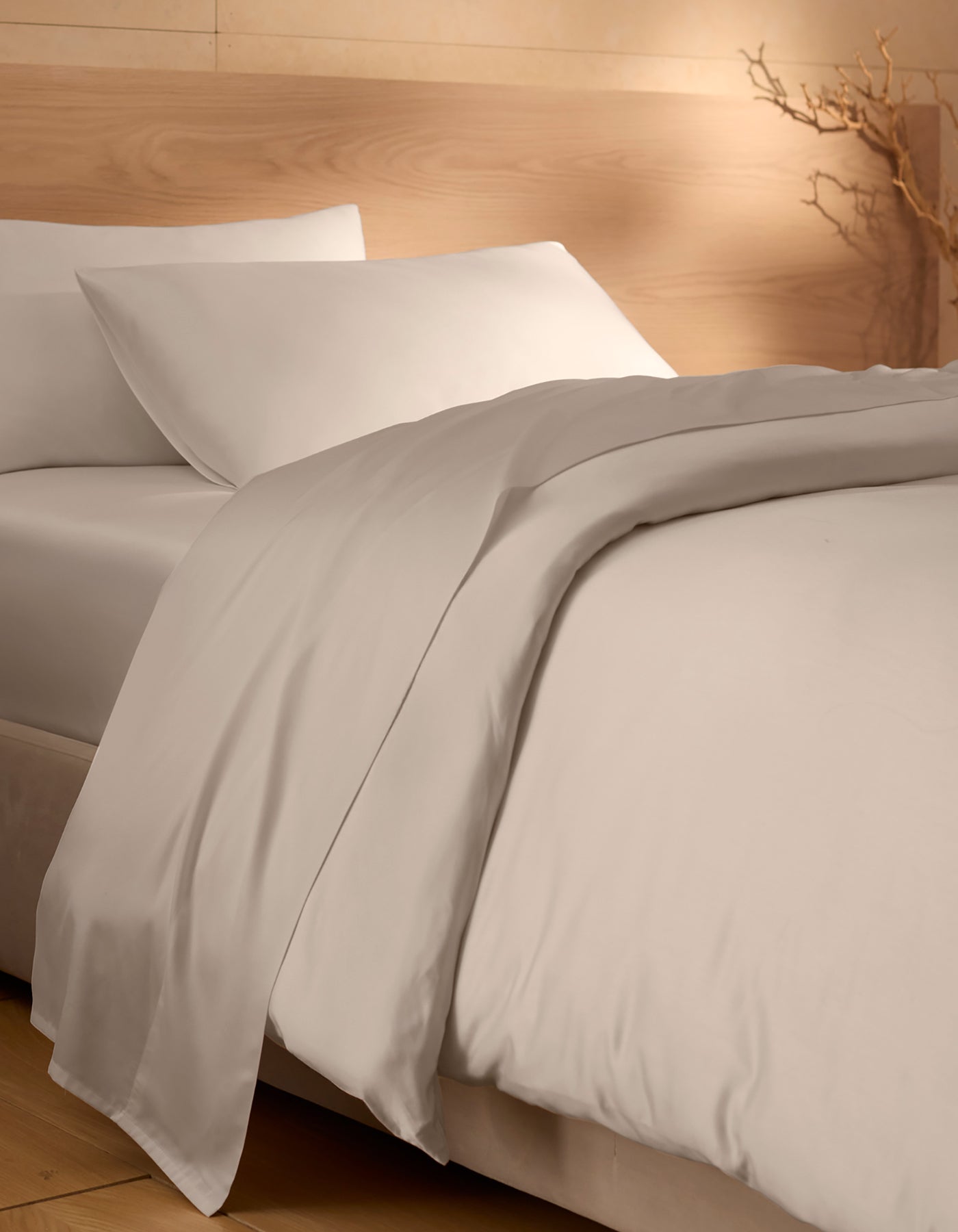 A neatly made bed featuring Cozy Earth's Bamboo Duvet Cover; beige walls, natural wood accents, and a dried branch in the corner create a calm, minimalist atmosphere.