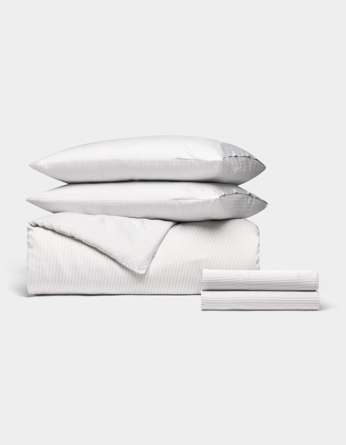 The Cozy Earth Bamboo Bedding Deluxe Bundle features a neatly arranged set with thin gray and white stripes, including two pillows, a folded comforter, and stacked sheets—all displayed against a plain white background.