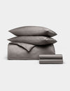 The Cozy Earth Bamboo Bedding Deluxe Bundle features neatly folded gray sheets, pillowcases, a duvet cover, flat and fitted sheets, and two stacked pillows displayed on a plain white background.|Color:Charcoal