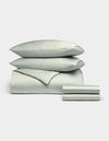 The Cozy Earth Bamboo Bedding Deluxe Bundle features a pale green set with two stacked pillows, a comforter, and folded sheets, elegantly displayed against a plain light background.|Color:Laurel