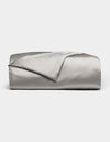 A neatly folded Cozy Earth Bamboo Duvet Cover in light gray is displayed against a white background, with one corner turned back to reveal its smooth, shiny fabric.|Color:Light Grey