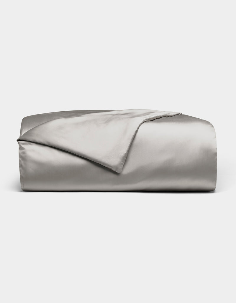A neatly folded Cozy Earth Bamboo Duvet Cover in light gray is displayed against a white background, with one corner turned back to reveal its smooth, shiny fabric.