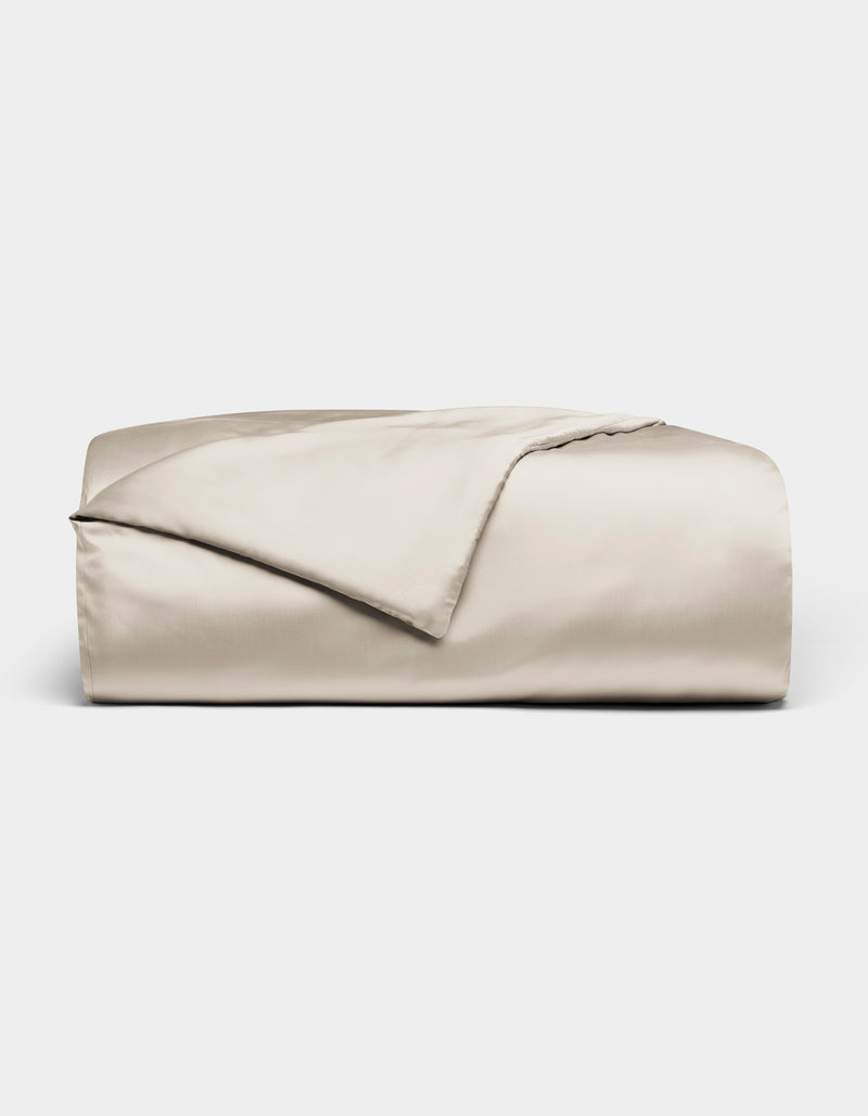 The Bamboo Duvet Cover by Cozy Earth, in light beige with a smooth satin finish, is neatly folded and displayed against a plain white background.