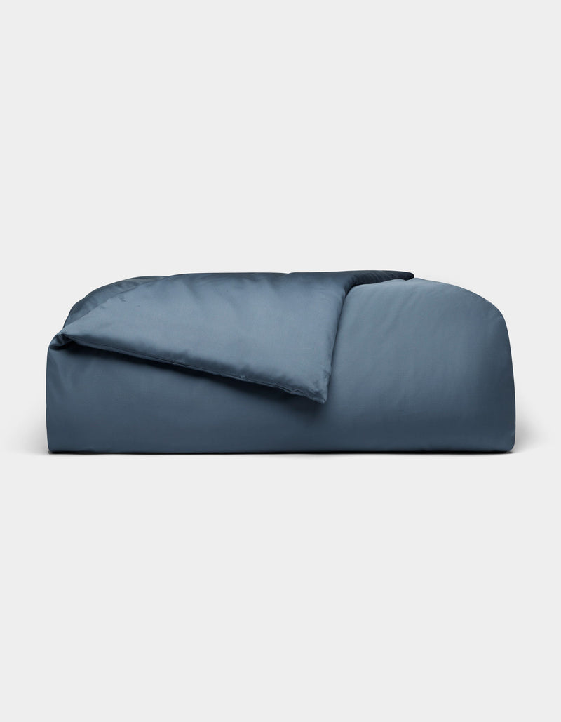 The Cozy Earth Bamboo Duvet Cover, in dark blue and rectangular shape, features plush fabric with a partially folded comforter, displayed against a plain light gray background.