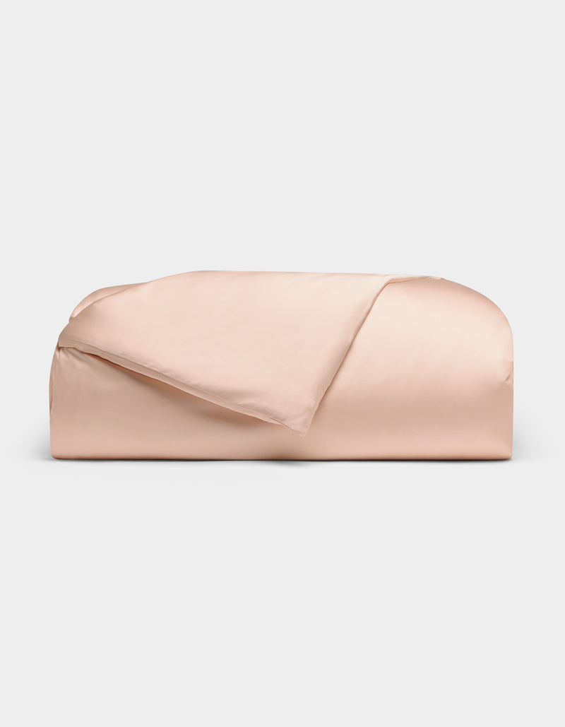 The Cozy Earth Bamboo Duvet Cover, in pale pink, is neatly folded against a plain white background with one corner turned down to reveal its smooth fabric.