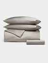The Cozy Earth Bamboo Bedding Essential Bundle features neatly folded light gray bedding—a comforter, two stacked pillows, and a rolled sheet—displayed on a plain white background.|Color:Dove Grey