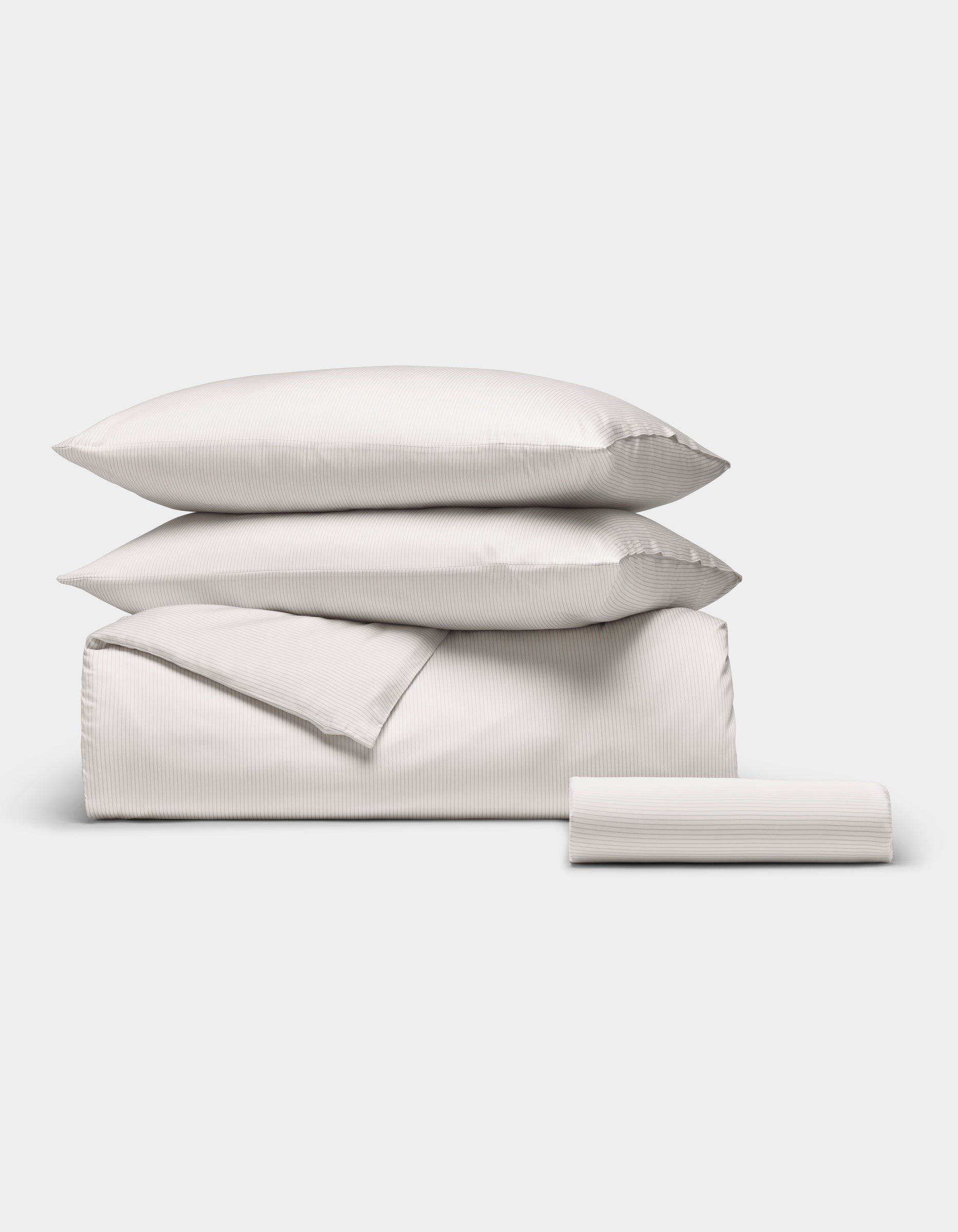 The Cozy Earth Bamboo Bedding Essential Bundle features two pillows, a folded sheet, and a rolled sheet in subtle striped light gray, neatly arranged on a plain white background.