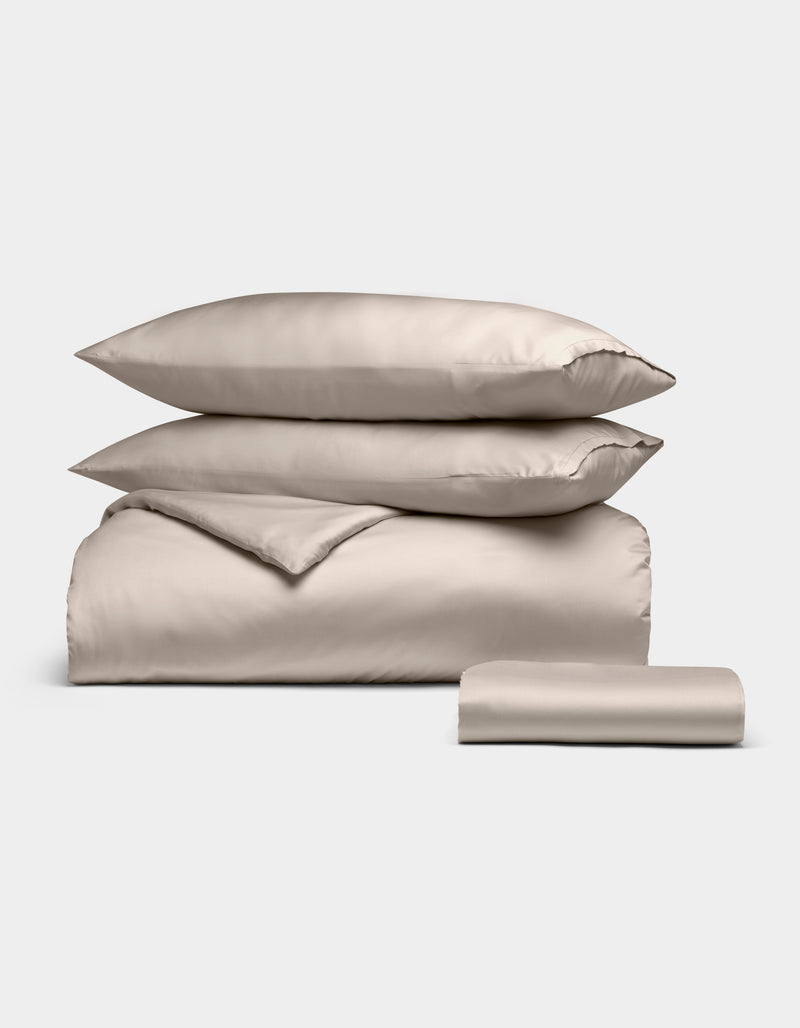 The Cozy Earth Bamboo Bedding Essential Bundle includes two pillows, a folded duvet, and a folded sheet in beige, all neatly stacked against a plain white background.