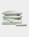The Cozy Earth Bamboo Bedding Essential Bundle, featuring two pillows, a folded duvet, and a sheet in pale gray, is neatly stacked against a plain white background.|Color:Laurel