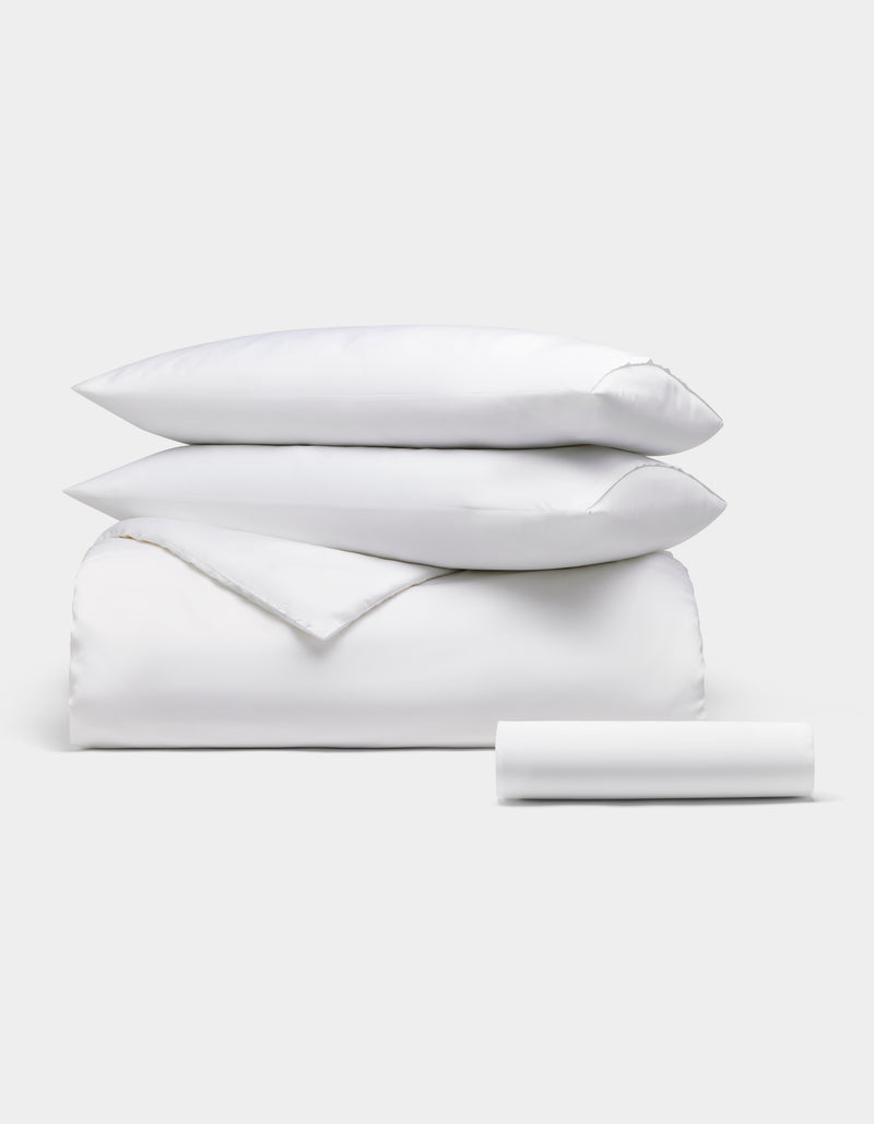 The Cozy Earth Bamboo Bedding Essential Bundle is neatly displayed: two pillows stacked on a folded comforter, with a rolled bedsheet in front, all set against a plain light background.
