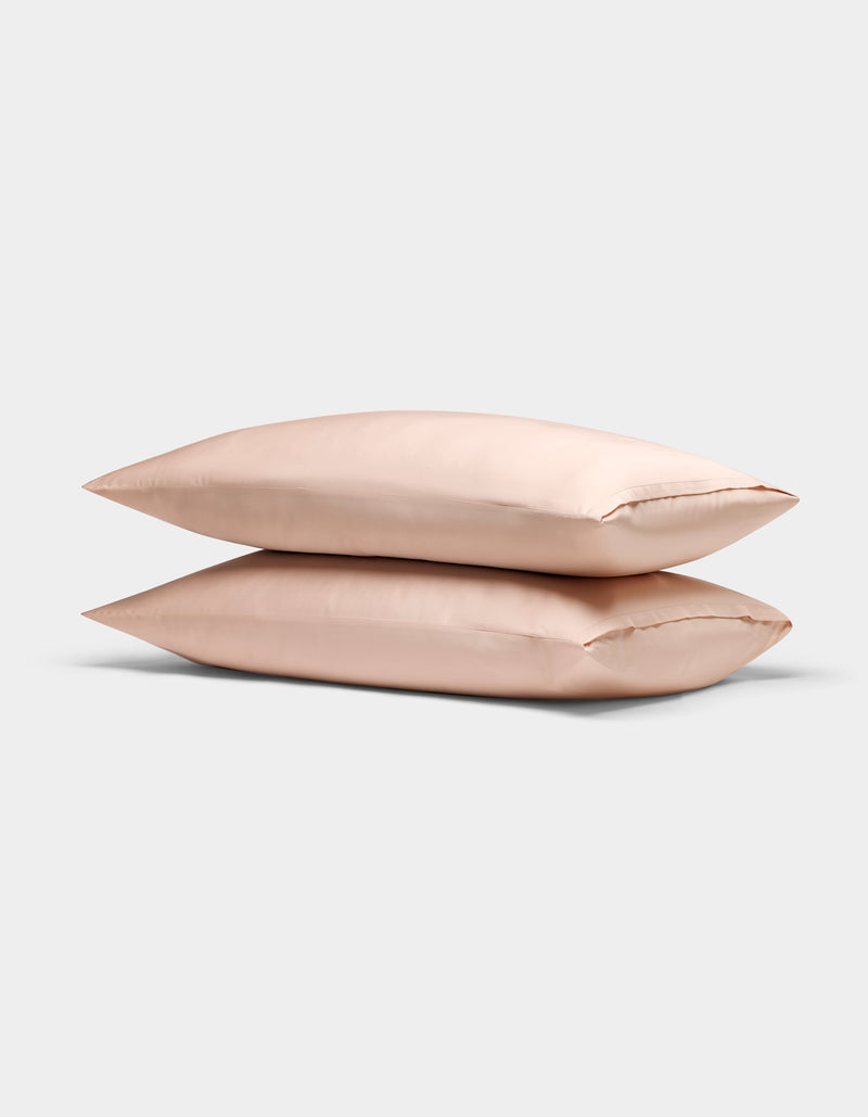 Two light pink Cozy Earth Bamboo Pillowcases are stacked neatly atop each other against a plain, light gray background.