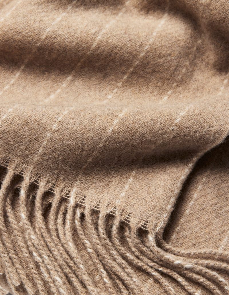 A close-up of the Florence Throw by Cozy Earth, featuring soft, light brown wool with thin white stripes and fringed edges. The texture and weave of this elegant blanket are clearly visible.