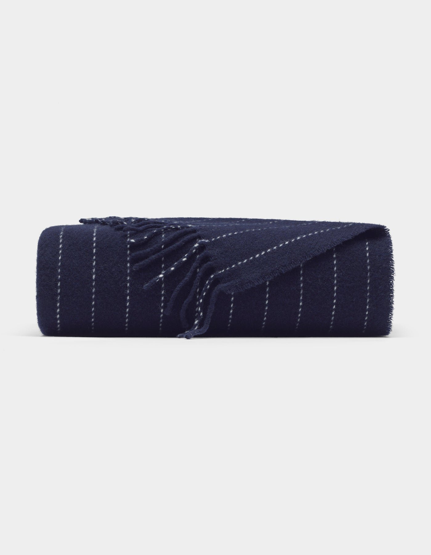 The Florence Throw by Cozy Earth is a navy blue blanket featuring thin, evenly spaced white stripes and fringed edges, shown neatly rolled on a plain white background.