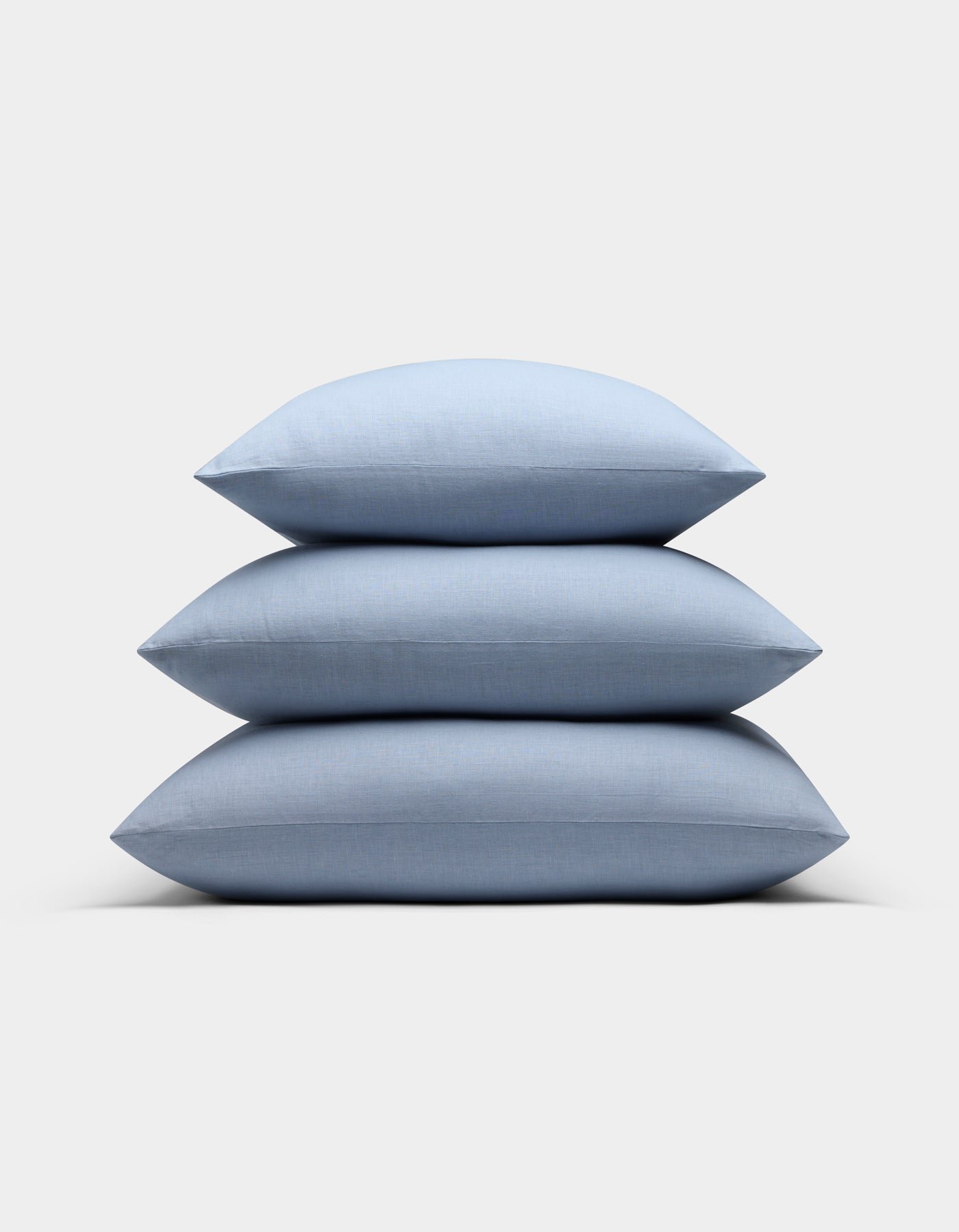 Three Cozy Earth Linen Throw Pillows in light blue are stacked neatly on top of each other against a plain white background.