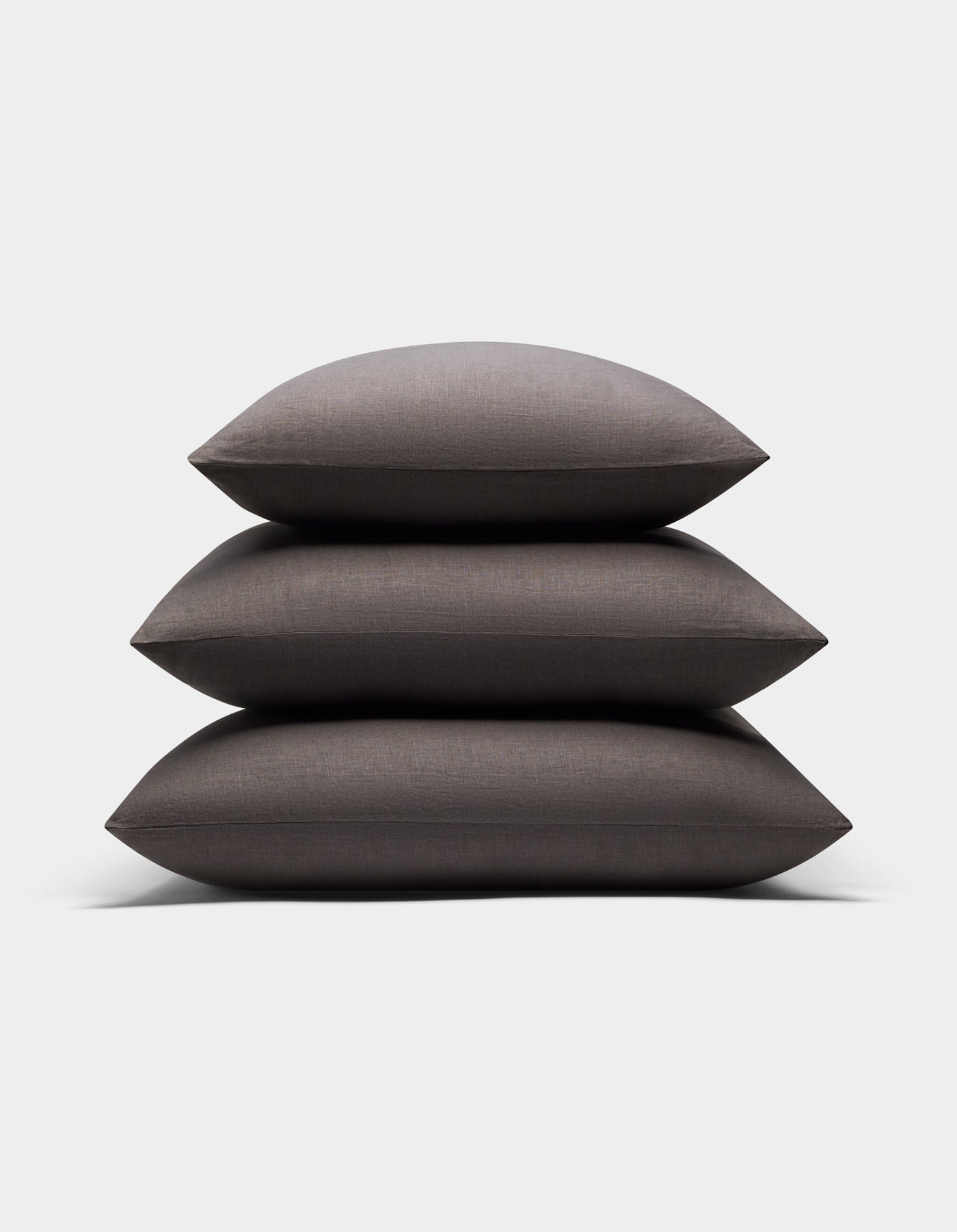 Three Cozy Earth Linen Throw Pillows in dark gray are stacked neatly against a light gray background. The pillows feature a soft, smooth fabric texture.