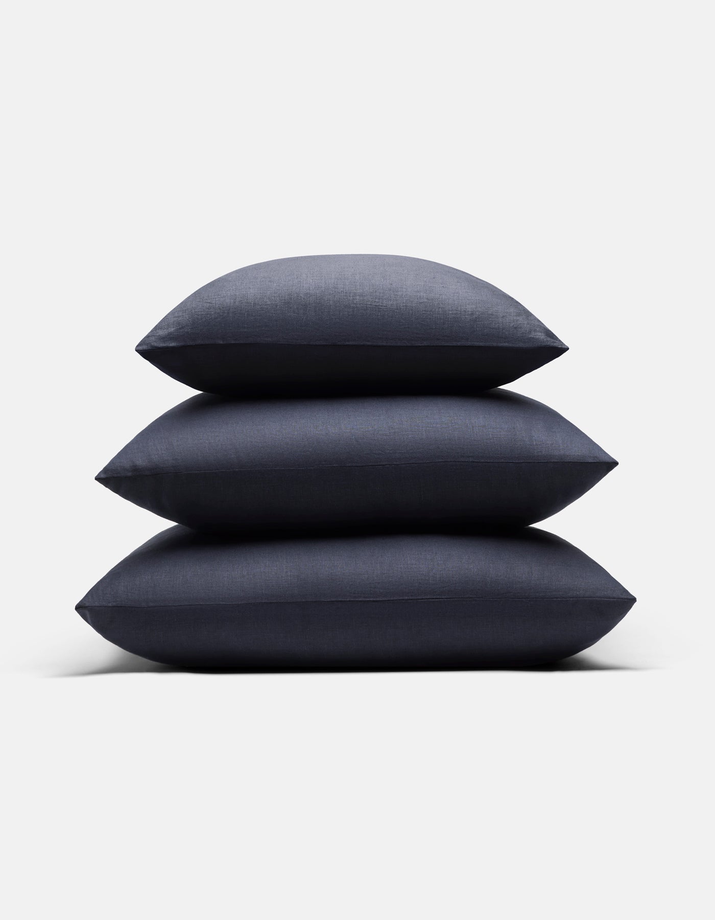Three Cozy Earth Linen Throw Pillows in dark blue are stacked neatly on top of each other against a plain white background.