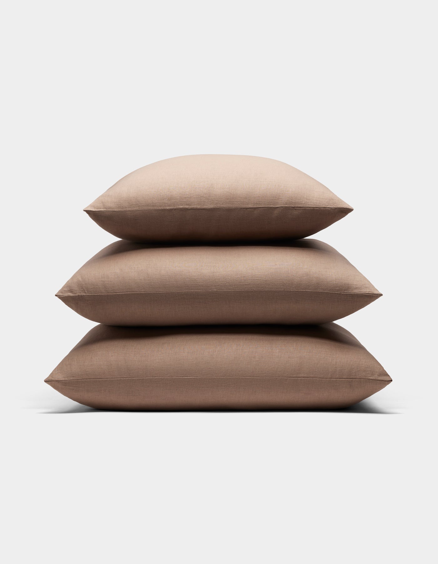 Three Cozy Earth Linen Throw Pillows in light brown are stacked neatly on top of each other against a plain white background.