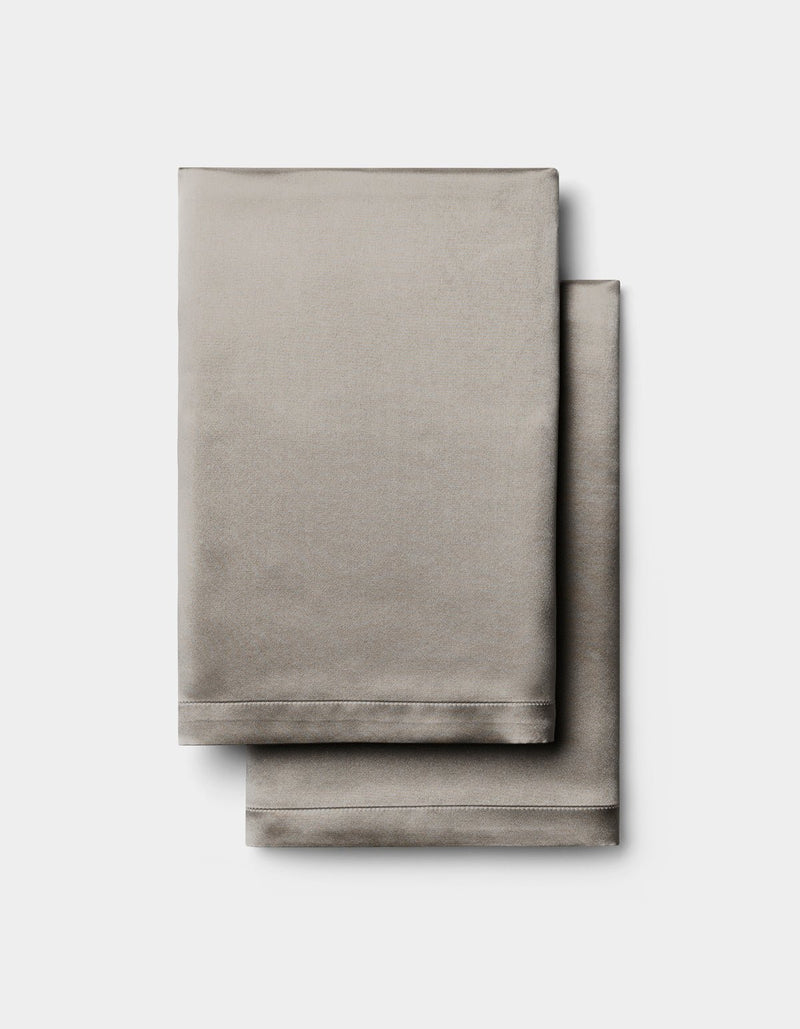 Two neatly folded Cozy Earth Silk Pillowcases in light gray are stacked together against a plain white background.