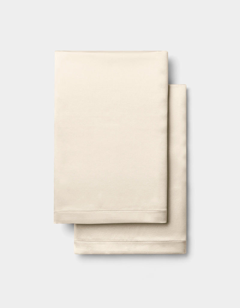 A folded Cozy Earth Silk Pillowcase in beige is stacked on a light gray background.